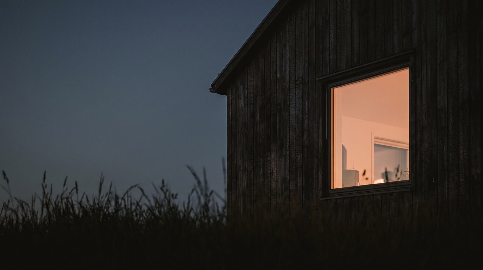 A single warm window glowing in a dark timber wall at dusk